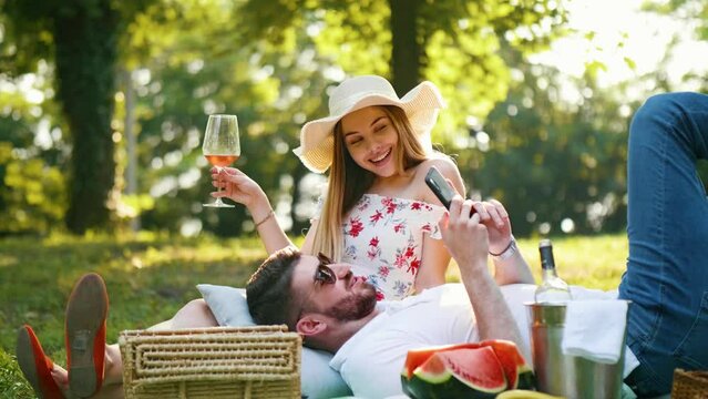 Young couple in the park on a picnic, enjoying and relaxing with wine and surfing the internet
