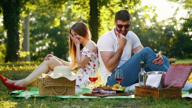 Happy boyfriend feeding her girlfriend on a picnic in city park. Young couple is having fun and laughing while spending time in nature