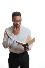 Afrodecent man with glasses focused reading a notebook. Isolated person on white background. Young man with turtleneck and hand on face.