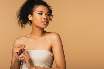 curly african american woman with bare shoulders looking away isolated on beige.