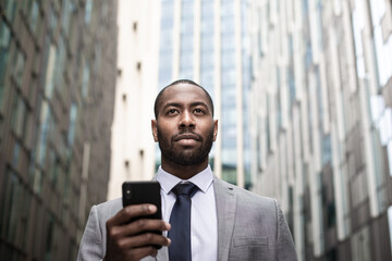 African American businessman walking in city using smartphone