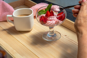 Woman's hand holds teaspoon with dessert of strawberries and whipped cream. Mature woman enjoys dessert of strawberries and whipped cream. Fragment. Topic - desserts