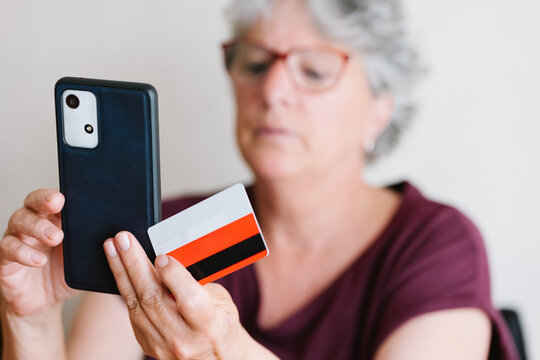 Happy senior lady using smartphone while paying for online shopping with credit card