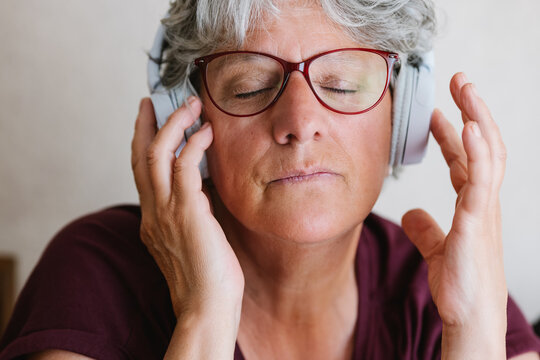 Satisfied senior lady listening to music in headphones with closed eyes