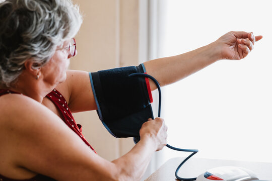 Anonymous elderly woman measuring blood pressure with electronic device at home