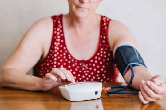 Anonymous elderly woman measuring blood pressure with electronic device at home
