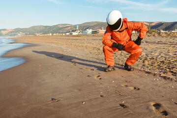 Unrecognizable cosmonaut examining footprints on sand