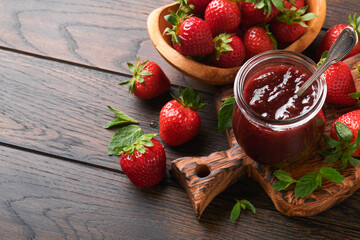Strawberry jam. Strawberry jam in glass jar with fresh berries plate on an old wooden dark table background, closeup. Homemade strawberry fruity jam. Top view with copy space.