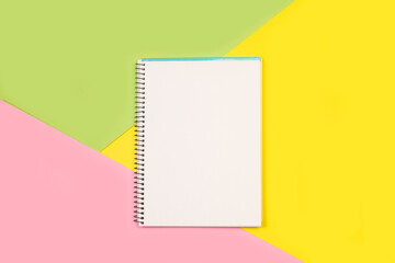 Cuaderno en blanco sobre un fondo de colores rosa, amarillo y verde. Vista superior y de cerca. Copy space
