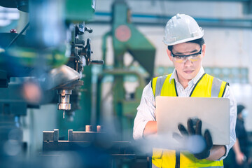 The white safety helmet engineer use laptop for a lathe for shaping the steel for a part follow blueprint in the laptop machinery in the factory industrial