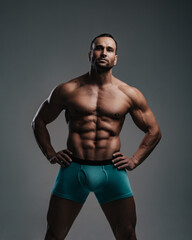 Fototapeta na wymiar Muscular sexy guy in turquoise shorts standing with hands on his belt in studio
