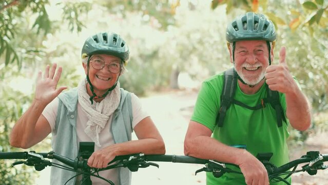 Two happy old mature people enjoying and riding bikes together to be fit and healthy outdoors. Active seniors having fun training in nature. Portrait of one old man smiling in a bike trip with his wif