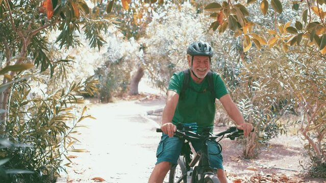 Two happy old mature people enjoying and riding bikes together to be fit and healthy outdoors. Active seniors having fun training in nature. Portrait of one old man smiling in a bike trip with his wif