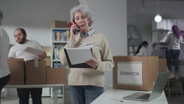 Mature woman with clipboard talk on phone discussing donation delivery