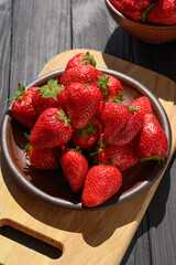 Plate of red juicy strawberries on a rustic wooden table. The concept of healthy and dietary snacks.