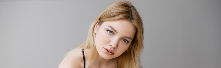 Portrait of blonde woman looking at camera isolated on grey, banner.