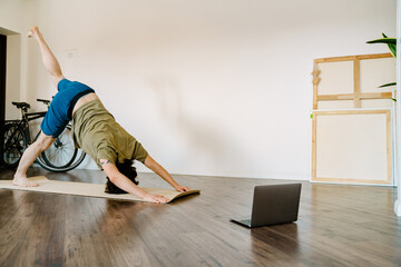 White man doing exercise during yoga practice with laptop