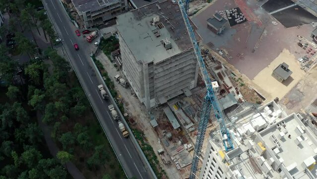 Construction of new apartments in the city near the park. Reconstruction and restoration of the city. Construction of multi-storey houses: construction site with crane and builders: drone shot.