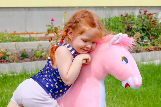 a little girl hugs a toy pink horse. playing in the yard. happy childhood. favorite toy. rocking horse