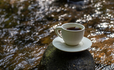 Obraz na płótnie Canvas Black coffee in a white cup on a stone in the middle of the river
