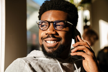 Black bearded man talking on mobile phone and smiling in cafe