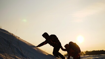 teamwork concept. help you partner climb snowy mountain with backpack. hiking winter mountains. walk together hand hand hill sunset. help path victory success. concept teammate with backpack sunlight - obrazy, fototapety, plakaty