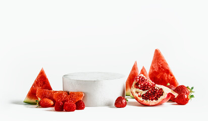 Empty podium with red fruits at white background. Stage for your product with watermelon slices, pomegranate seeds, raspberries, strawberries and grapefruit. Front view with copy space.