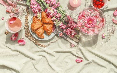 Aesthetic summer sunny breakfast picnic with croissants, flowers, tea and cherries at pale beige blanket. Top view.