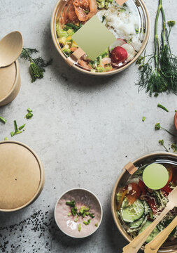 Healthy salads lunch in sustainable packaging with empty label mock up at grey table background with herbs and biodegradable food containers. Delicious to go poke bowls. Top view with copy space.