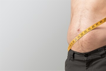 A young guy wearing a big jeans and measuring his waist by a tape measure over background.