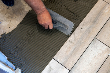 Builders laying tiles on concrete floor with notched trowels, level and tile mortar
