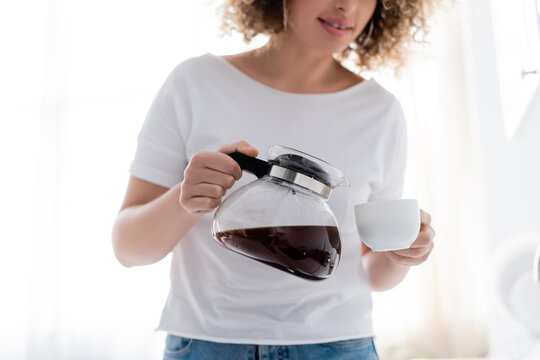 cropped view of curly woman in white t-shirt pouring morning coffee.