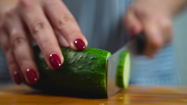 Women cuts a cucumber with a knife