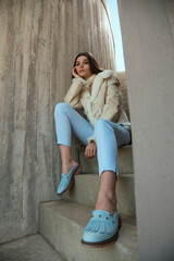 fashion model in light blue pants and fur jacket posing on the stairs