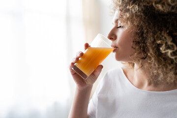 young woman with curly hair drinking fresh orange juice at home.