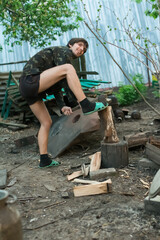 A man in military uniform is chopping wood. Sunny day in the countryside.