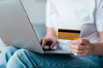 partial view of woman with credit card using laptop on blurred background.