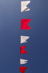 Um varal com bandeirolas nas cores vermelha e branca com c&eacute;u azul ao fundo.