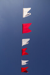 Um varal com bandeirolas nas cores vermelha e branca com c&eacute;u azul ao fundo.