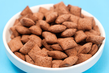 Sweet breakfast cereal dry - chocolate pads made of cereals on a blue background, side view