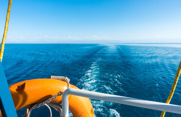 Ship's stern, lifeline. Footprint on the water from the boat. Blue water and mountains on the horizon. Issyk-Kul, Kyrgyzstan.