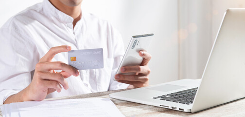 A smart and handsome young man at home office or co-working space using a credit card and smartphone for ordering online shopping. Technology money wallet and transferring money app payment concept