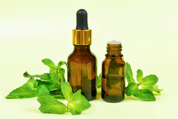 Essential oil of mint (peppermint) in a dark glass bottle with a pipette and a dispenser on a yellow background. Aromatherapy (against fatigue, headache, relaxation), spa, skin care.