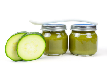 Baby food. Two glass jars with baby squash puree (zucchini) and a spoon on a white insulated background. The first lure of the baby.
