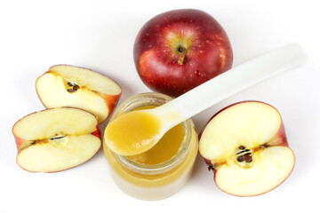 Baby food. A glass jar with baby apple puree with a spoon and red ripe apples on a white isolated background. The first fruit lure of the baby.