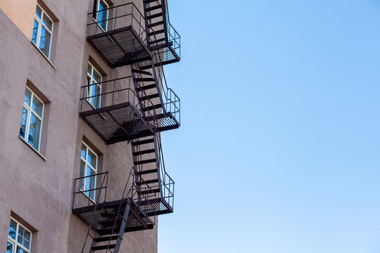 Silhouette of a fire escape on a high-rise building against a blue sky with clouds. Some of the stairs are broken. There is free space for text - Powered by Adobe