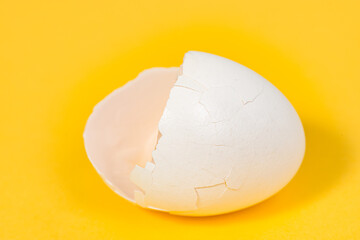 Close up of a cracked white egg shell with a shallow depth of field isolated on yellow