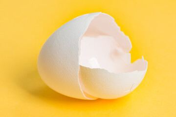 Close up of a cracked white egg shell with a shallow depth of field isolated on yellow