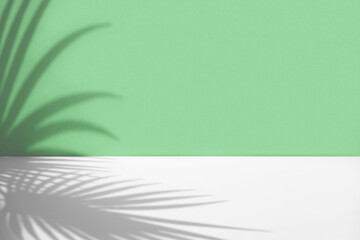 Minimal abstract background with shadow of tropical palm leaves. Presentation of cosmetic product. Premium podium on pastel light green wall and white table. Showcase, display case, Front view. Mockup