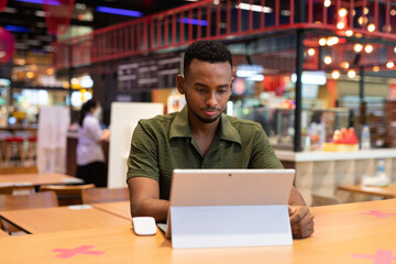 Obraz premium Portrait of handsome young black man using laptop computer in coffee shop